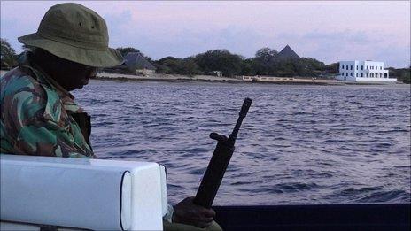 Kenyan soldier with Marie Dedieu's thatched cottage in the background