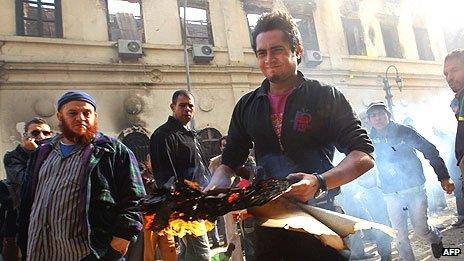 Мужчина выносит горящие книги из разрушенного Института Египта