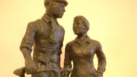 Miniature model of a statue showing man pushing a bike alongside a woman