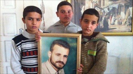 The three al-Haddar brothers hold up a portrait of their father