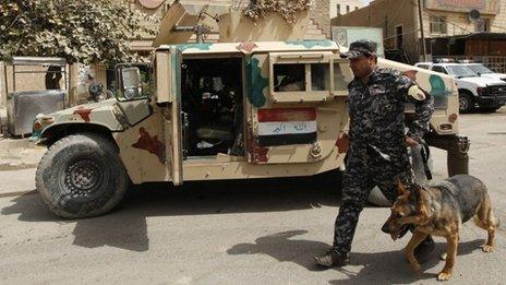 A police officer walks a sniffer dog at a checkpoint in Baghdad (26 March 2012)