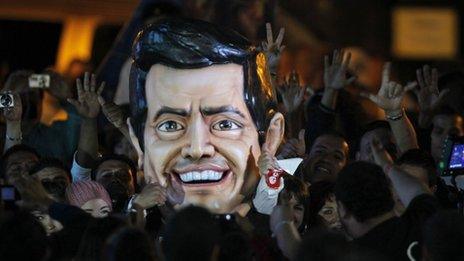 A large figure of Enrique Pena Nieto's head surrounded by crowds at a rally
