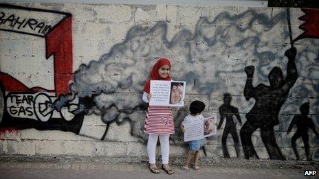 Bahraini children hold up pictures of activists allegedly tortured by security forces in Bahrain, behind graffiti demanding the cancelling of Sunday's Grand Prix (19 April 2011)
