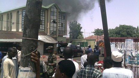 People gather as smoke billows out of the ThisDay building in Kaduna