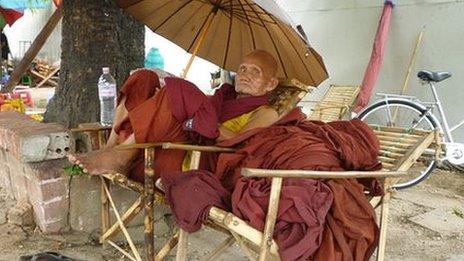 Elderly Burmese monk sits under sunshade