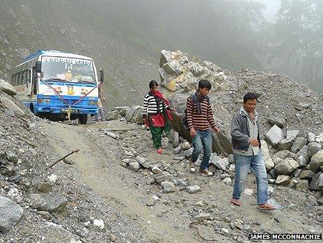 Three people walk downhill in front of a bus