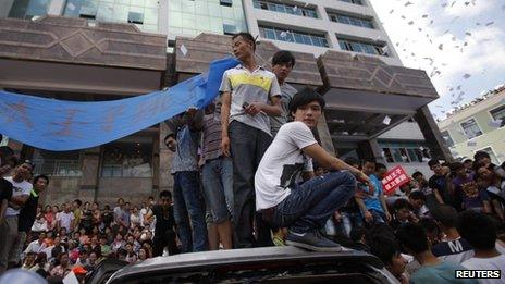 Local residents stand on smashed cars as they occupy the local government building during a protest against an industrial waste pipeline under construction in Qidong
