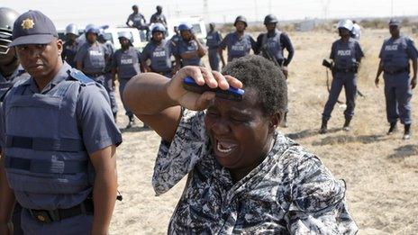 A local women cries as she confronts a police officer during a protest against the killing of miners by South African police