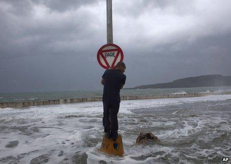 A man clings to a stop sign as waves pass over the seawall in Baracoa, Cuba, 25 August