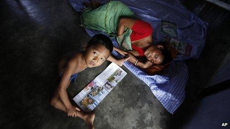 An Indian riot refugee woman sleeps as her child reads a book at a relief camp during India’s ruling Congress party President Sonia Gandhi visit in Deborgaon in Kokrajhar, India, Monday, Aug. 13, 2012