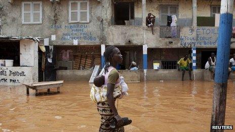 A woman with a baby on her back wades through water after overnight flooding on a street in Senegal's capital Dakar, 14 August 2012