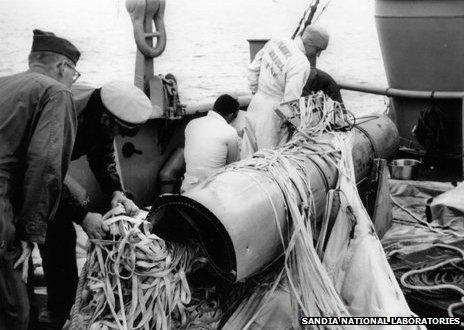 Navy personnel aboard USS Petrel examine weapon number 4, recovered from the sea bed and still tangled in its parachute
