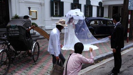 A photographer positions a bride for a picture for her wedding photo album in front of a colonial style hotel, rickshaw and old cars in downtown Hanoi on August 26, 2010.