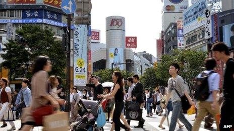 Pedestrians cross a road in front of the Shibuya station in Tokyo on 21 June, 2011