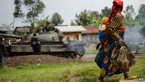 A displaced woman carrying her child walks past an army tank in eastern Democratic Republic of Congo (26 July 2012)