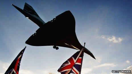 People wave Union Jack flags below a British Airways Concorde in silhouette