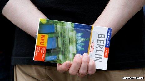 A man holding a Berlin travel guide behind his back