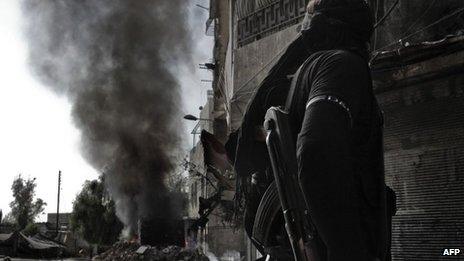 A rebel fighter looks at smoke billowing from a burning bus in Aleppo (28 October 2012)