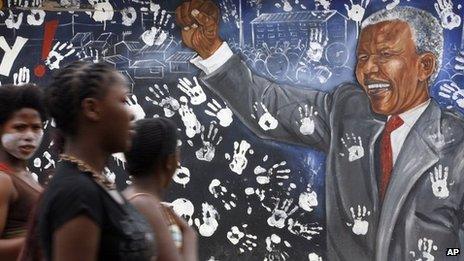 Young women walk by a mural depicting former South African President Nelson Mandela at Alexandra township in Johannesburg, South Africa, on Tuesday 11 December 2012