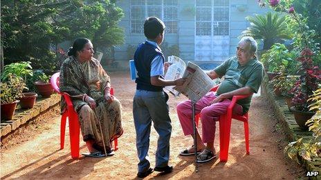 A delivery boy gives a newspaper to a 66-year-old Anglo-Indian resident of McCluskieganj, eastern India, as the man sits in his garden with his Indian wife, in October 2011