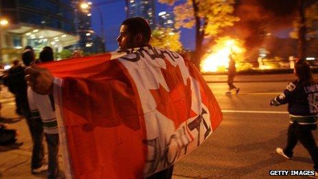 A rioter walks through Vancouver with a Canadian flag 15 June 2011