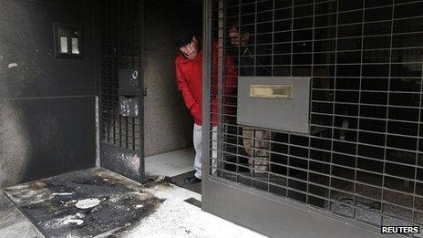 A resident stands at the burned entrance of a building following a series of arson attacks against journalists in Athens, 11 January 2013