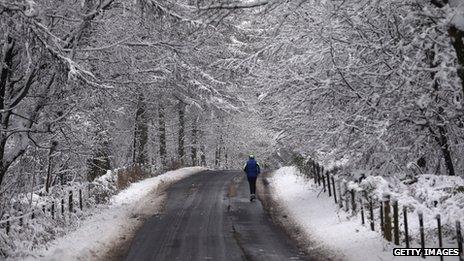 A man runs among the snow covered trees surrounding the grounds close to Stourhead