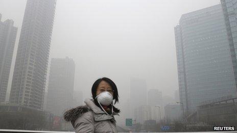 A woman wearing a mask walks on a pedestrian bridge on a hazy day in Beijing
