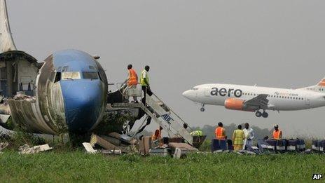 A passenger plane lands as workers dismantle an abandoned aircraft at Murtala Muhammed International Airport in Lagos, Nigeria, on 31 January 2013