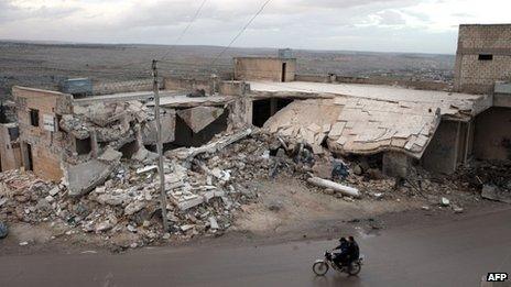 Syrians ride a motorcycle past the remains of a building allegedly destroyed by an explosive device dropped from a Syrian warplane in the town of Kfar Nubul, Idlib province (11 February 2013)