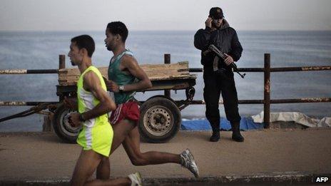 A picture taken on May 5, 2011 shows a Hamas policeman talking on the phone as Palestinian Olympic athlete Nader Masri (L) and a fellow runner speed along the waterfront in Gaza City