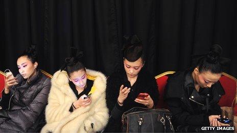 Four women look at mobile phones while sitting next to each other