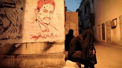 A tear-gassed woman sits next to a mural of jailed activist Abdulhadi al-Khawaja
