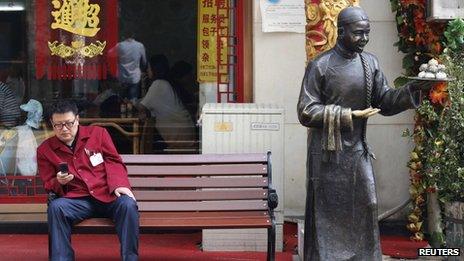 A man sits on a bench in front of a restaurant at a shopping district in Beijing