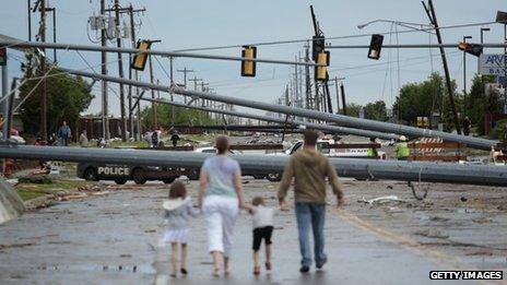 A family walks a street blocked by fallen utility poles in Moore, Oklahoma, on 21 May 2013