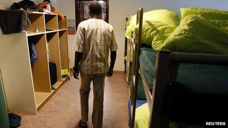 An asylum seeker walks past beds in a sleeping room of the asylum centre "Les Pradieres" for refugees during a tour for media in Val-de-Ruz near Neuchatel