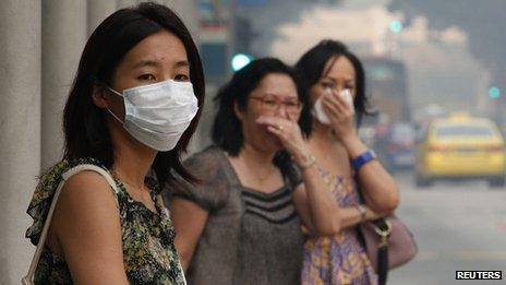 Commuters cover their mouths as they wait to cross a road in the haze in Singapore on 20 June 2013