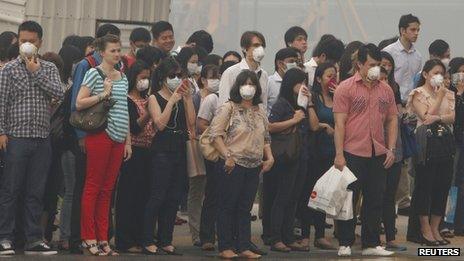 Office workers wearing masks wait to cross a road in Singapore on 21 June 2013