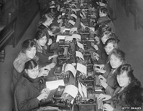 Female workers sit in two long rows in front of typewriters