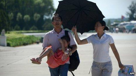 A woman (R) holds an umbrella over a man (L) as he holds his daughter while walking along a street in Beijing, 28 July 2013