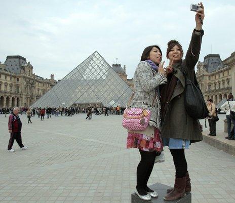 Tourists pose in front of the Louvre