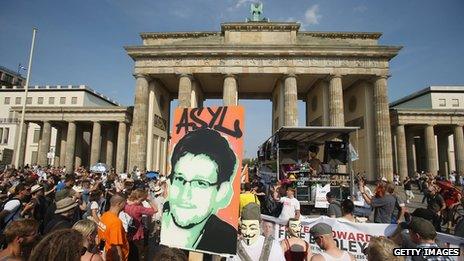 A participant holds up a picture of former Edward Snowden with the word "asylum" written above it at a protest gathering in front of the Brandenburg Gate on July 27, 2013 in Berlin, Germany