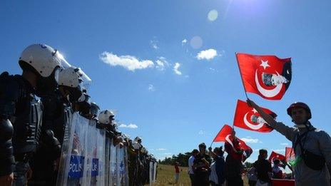 Protesters waves posters of Turkey's founder Kemal Ataturk at a riot police barricade as security block thousands of people outside the Silivri jail complex in Silivri, Turkey, Monday, Aug