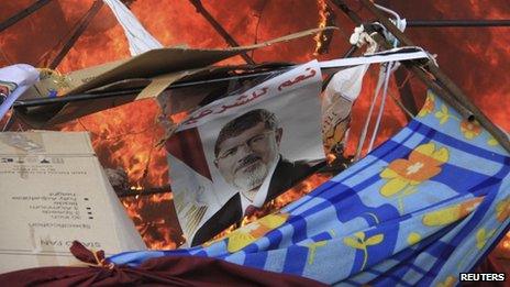 A poster among flames as riot police clear supporters of deposed Egyptian President Mohammed Morsi from a camp at Rabaa al-Adawiya square in Cairo on 14 August 2013