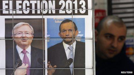 A man walks behind an advertisement for a newspaper with pictures of Australian Prime Minister Kevin Rudd (L) and opposition leader Tony Abbott in central Sydney, 5 August 2013