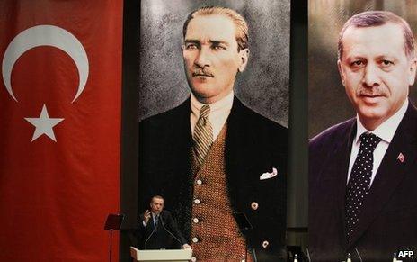 Erdogan gestures as he gives a speech under a Turkish flag and portraits of himself and Ataturk