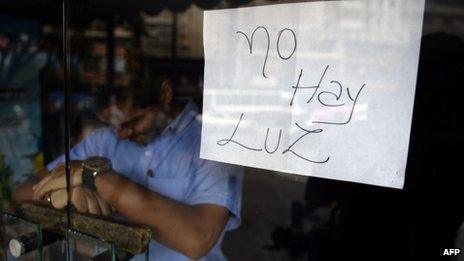 An employee of a business closed during a blackout stands behind the door with a notice reading "There's No Electricity", in Caracas on 3 September, 2013