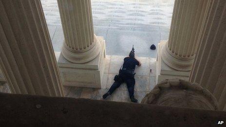 A US Capitol police officer lies on the steps of the Senate with a gun drawn in response to a report of shots fired