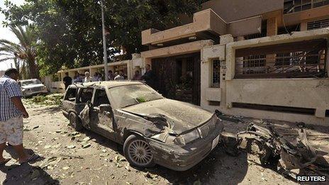 People look at a damaged car outside the Swedish consulate after a car bomb explosion, in Benghazi on 11 October 2013.