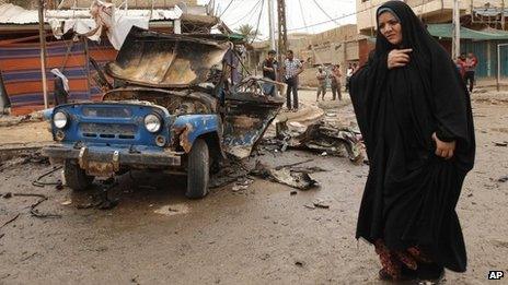 An Iraqi woman walks past a bomb-damaged vehicle in Baghdad (20 May 2013)